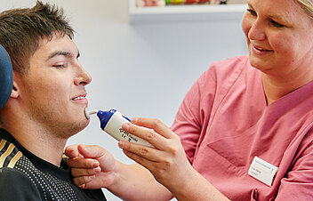 Bild: Die Therapeutin stimuliert mit einem Massagegerät die Mundpartie eines Patienten