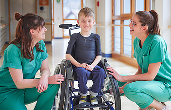 Bild: Zwei Therapeutinen kümmern sich um einen Jungen im Rollstuhl