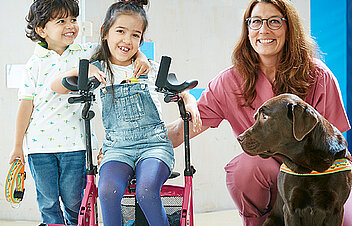 Bild: 2 kleine Patienten der Kinderklinik mit dem Therapiehund Fanny und der Therapeutin