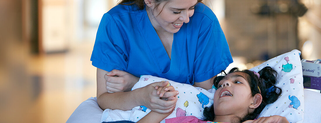 Bild: Eine Pflegefachkraft kommuniziert mit einer jungen Patientin, die Pflegerin hält die Hand der Patientin