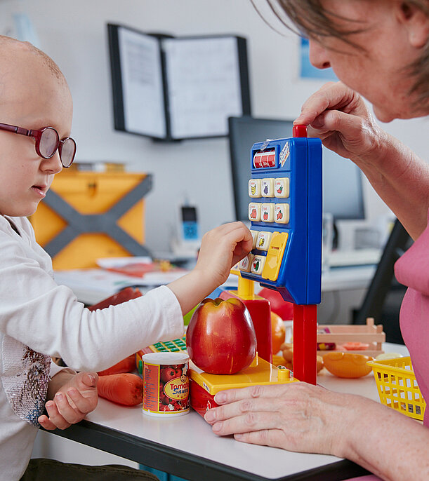 Action-oriented speech therapy Picture: Speech therapist and patient playing customer and merchant in a children's shop (action-oriented speech therapy)