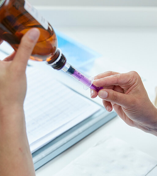 Bild: Eine pflegerische Mitarbeiterin bereitet eine Spritze mit einem Medikament in Saftform vor