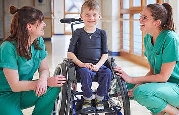 Bild: Zwei Therapeutinnen mit einem Kind im Rollstuhl. Das Bild ist verlinkt mit der Rubrik Mitarbeit in der Kinderklinik Schömberg