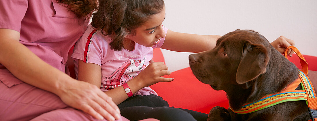 Bild: Mit Unterstützung seiner Therapeutin nimmt ein Patient durch Streicheln Kontakt zu einem Therapiehund auf