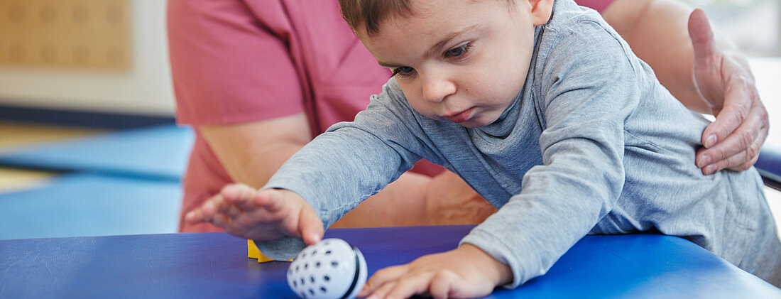 Bild: Die Physiotherapeutin weckt mit einem Spielzeug die Neugier eines Kleinkindes