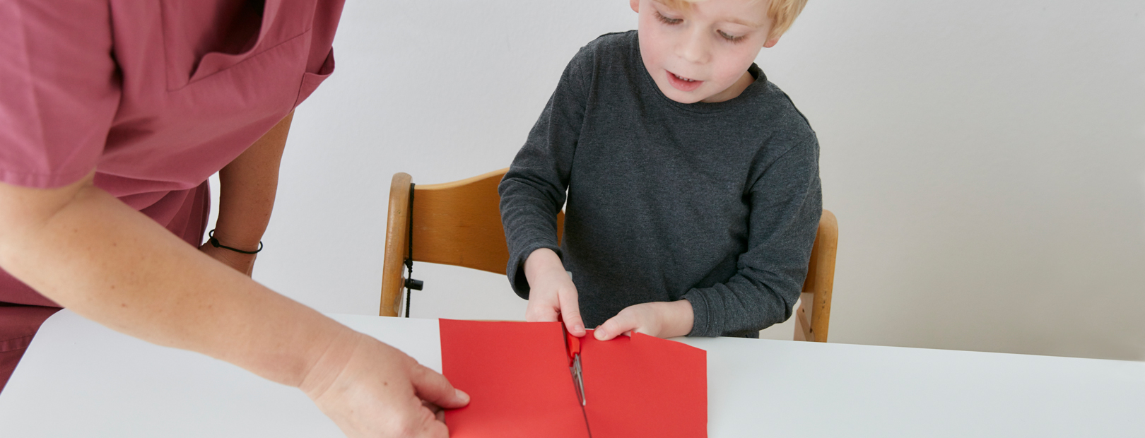 Occupational therapy diagnostics paediatric clinic Schömberg [Picture: Occupational therapy diagnosis. Under the guidance of a therapist, a small patient cuts a sheet of paper with scissors.