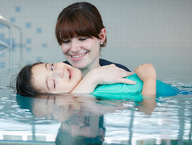 Picture: A small child with severe tonus regulation disorder relaxes in the warm water in the arms of his therapist.