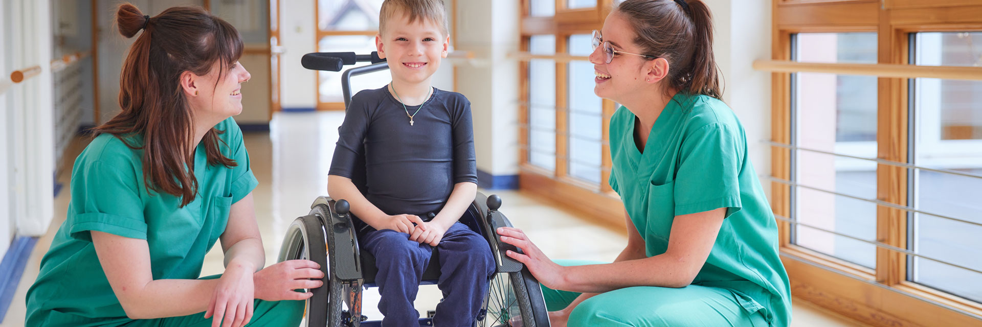 Bild: Zwei Pflegefachkräfte der Kinderklinik kommunizieren mit einem Jungen im Rollstuhl